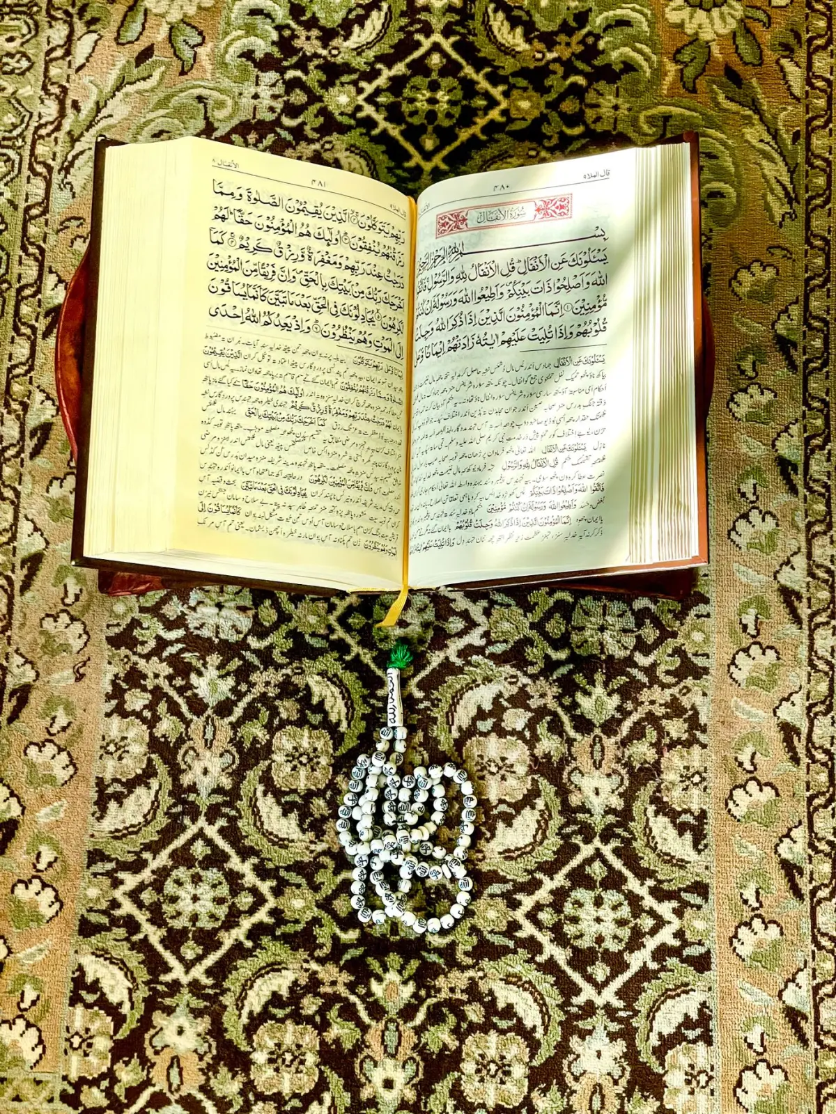 An open Quran and prayer beads arranged on a patterned prayer rug